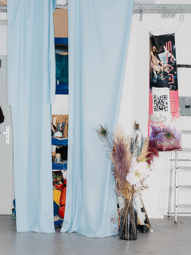 Two curtains hanging from wall to ceiling and hiding shelves, with a vase of dried flowers and grasses beside them