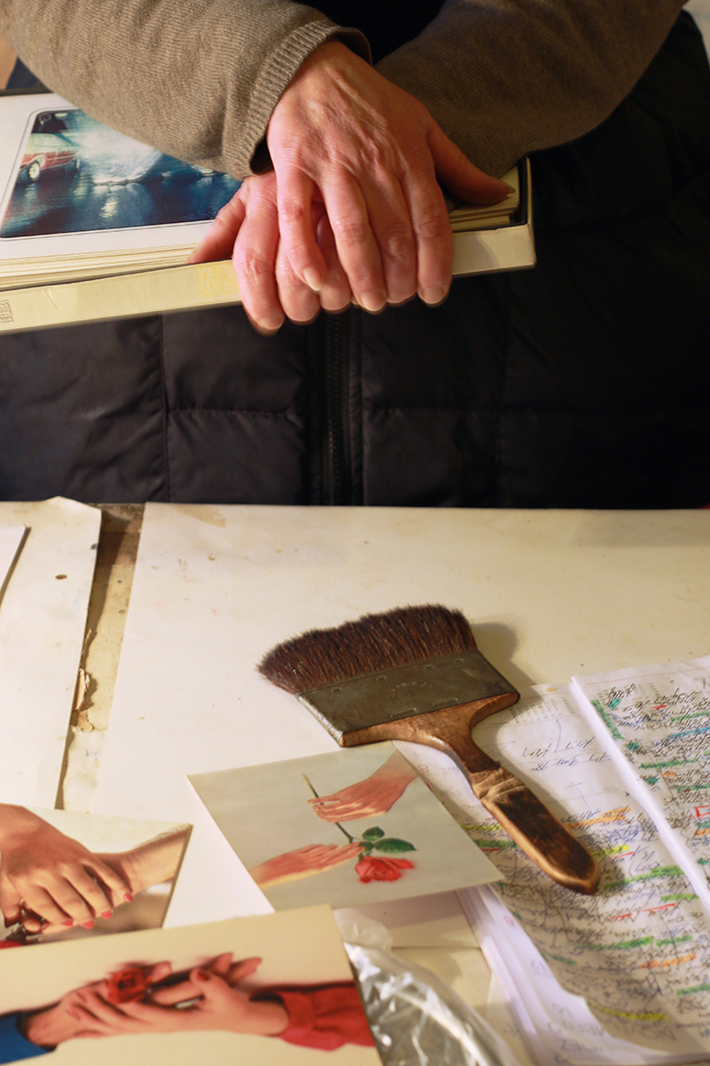 Frenzel holds a box of her photographic prints. On the table below her are postcards of people handing roses to each other